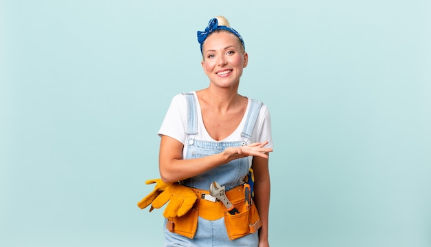 Bonita mujer rubia sonriendo alegremente, sintiéndose feliz y mostrando un concepto y reparando el concepto de casa