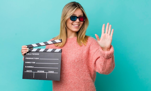 Bonita mujer rubia sonriendo y luciendo amigable mostrando el concepto de cine número cinco