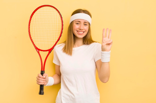 Bonita mujer rubia sonriendo y luciendo amigable mostrando el concepto de tenis número tres