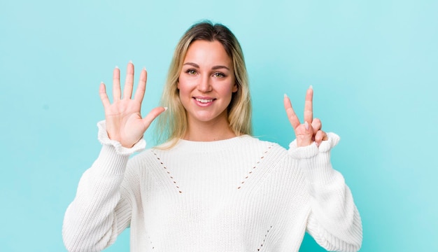 Bonita mujer rubia sonriendo y luciendo amigable mostrando el número siete o séptimo con la mano hacia adelante contando hacia atrás