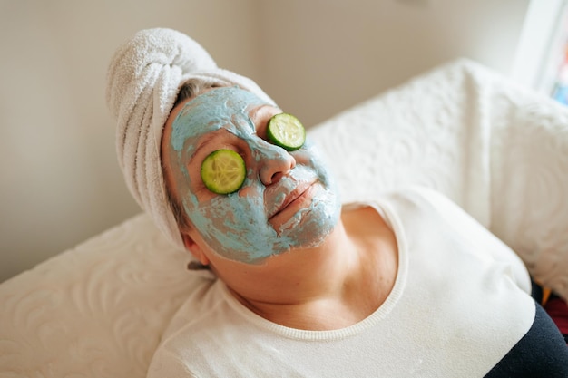 Una bonita mujer con sobrepeso tomando un momento para relajarse y disfrutar de su rutina de cuidado de la piel en casa en la foto auténtica y real lleva una máscara facial y tiene rebanadas de pepino en los ojos para un calmante