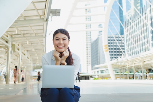 Bonita mulher asiática, sentada no chão com o laptop com o sorriso.