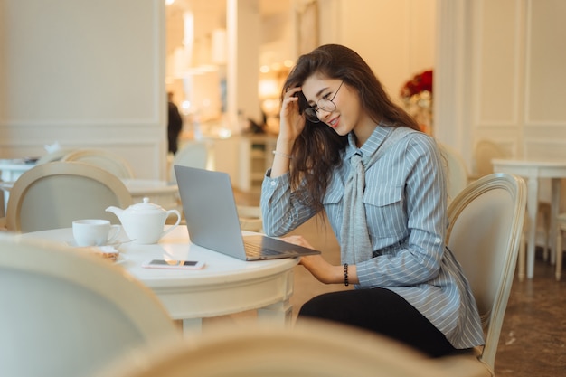 Bonita mulher asiática tomando uma xícara de chá enquanto estiver usando o computador portátil no café