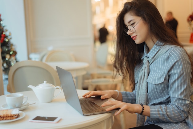 Bonita mulher asiática tomando uma xícara de chá enquanto estiver usando o laptop no restaurante