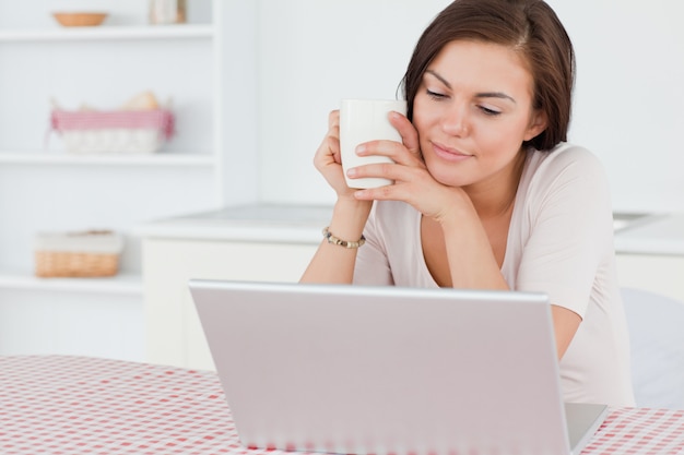 Foto bonita mulher darkhaired usando seu laptop e tomando um chá