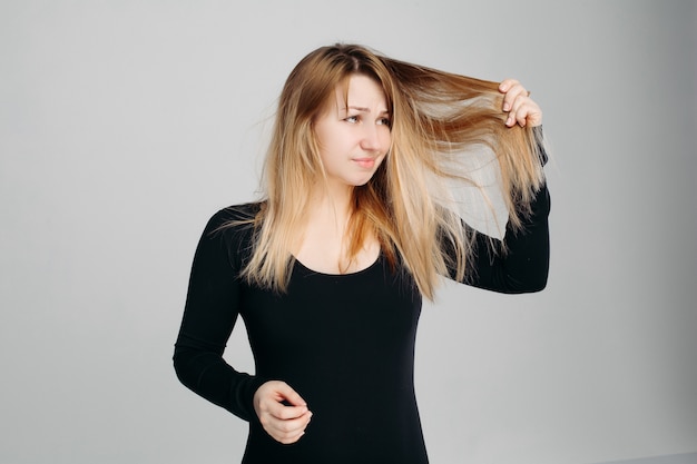 Bonita mulher segurando cabelo desarrumado em uma mão e escova de cabelo em outra