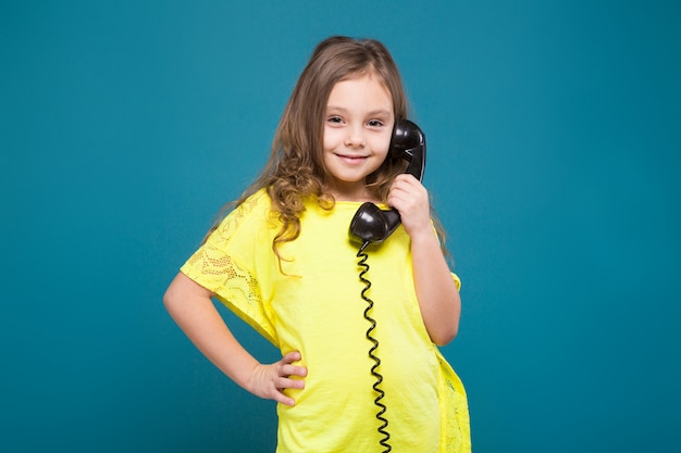 Bonita, niña en camiseta con el teléfono de pelo marrón espera