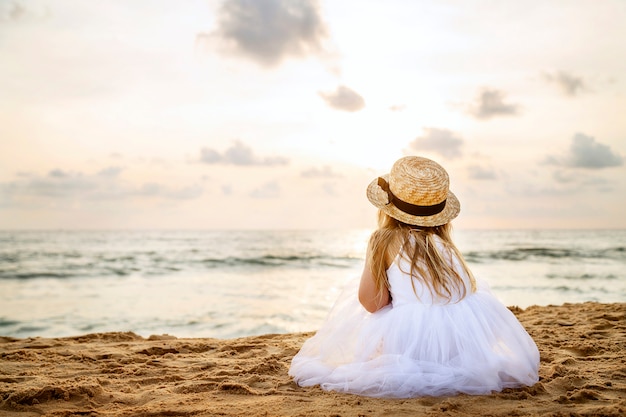 Bonita niña por detrás con cabello largo y rubio con un sombrero de paja y una sesión de vestido de tutú blanco