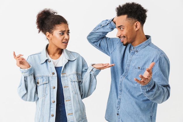 Bonita pareja africana en camisas de mezclilla disputas entre ellos sobre la pared gris