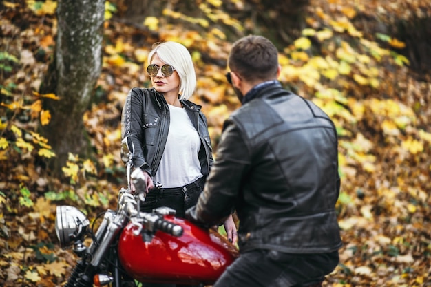 Bonita pareja cerca de motocicleta roja en la carretera en el bosque