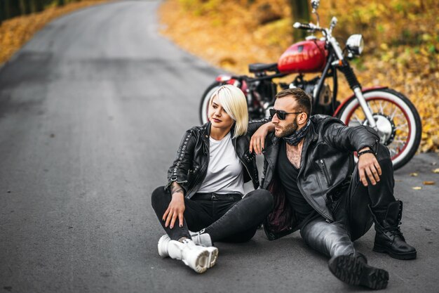 Bonita pareja cerca de motocicleta roja en la carretera en el bosque