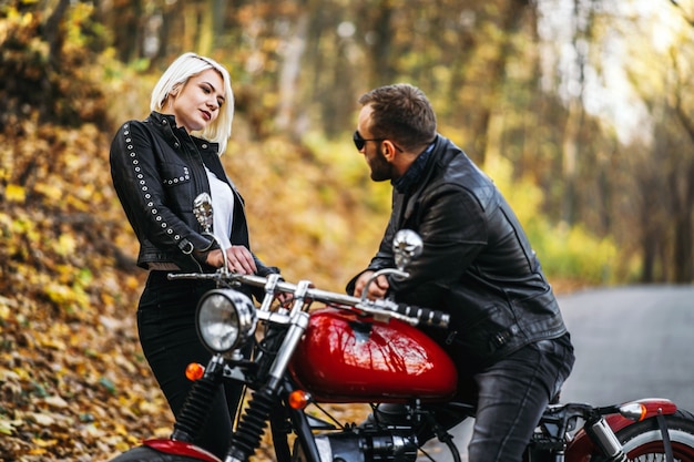 Bonita pareja cerca de motocicleta roja en la carretera en el bosque