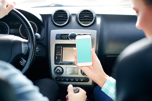 Bonita pareja sentada en un automóvil nuevo y sosteniendo un teléfono móvil.