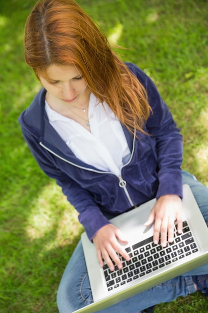 Bonita pelirroja relajante en el parque usando laptop