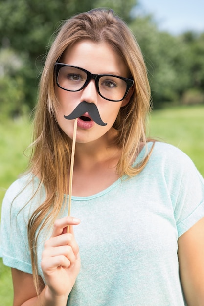 Bonita rubia sonriendo a la cámara con bigote falso