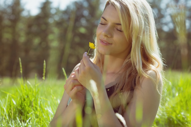 Bonita rubia en sundress sentado en la hierba con flor amarilla