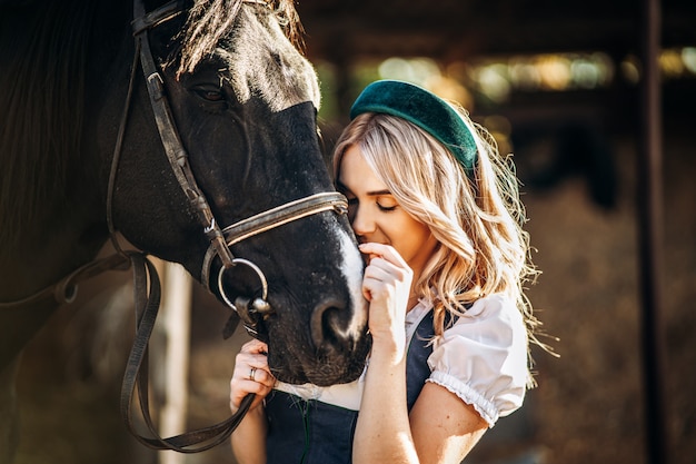 Bonita rubia con vestimenta tradicional cuida el gran caballo negro en la granja