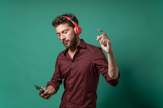 Bonitão em uma camisa ouve música com fones de ouvido sem fio - segurando um smartphone - conceito de tecnologia moderna, música e diversão