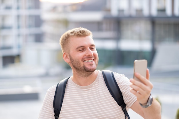 Bonito adulto de meia idade loiro barbudo roupas casuais tomando selfie na cidade ao ar livre com seu smartphone Sorrindo cara caucasiano feliz usando fotografia de rua por telefone