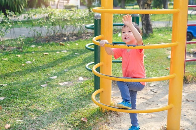 Bonito asiático 3 anos de idade criança bebê menino se divertindo tentando subir no quadro de escalada no playground ao ar livre