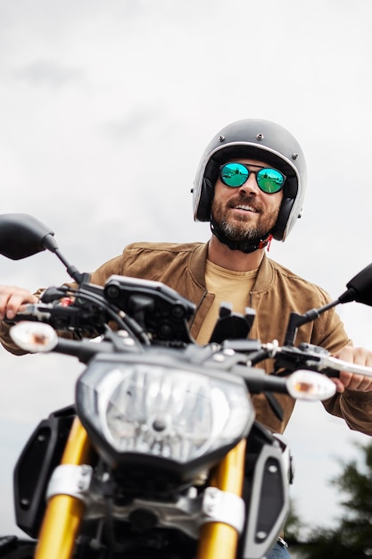 Foto bonito, barbudo, brutal, com óculos de sol elegantes, a andar de moto na estrada, aventura, liberdade, viagem de estrada.