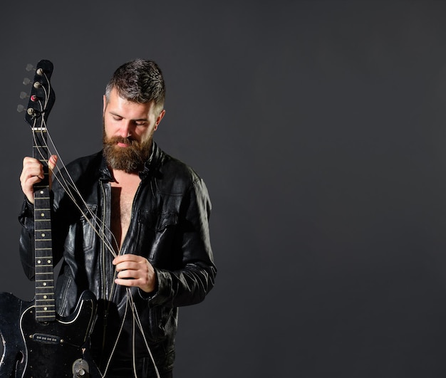 Bonito barbudo em uma jaqueta de couro com guitarra elétrica homem com barba segurando um instrumento musical