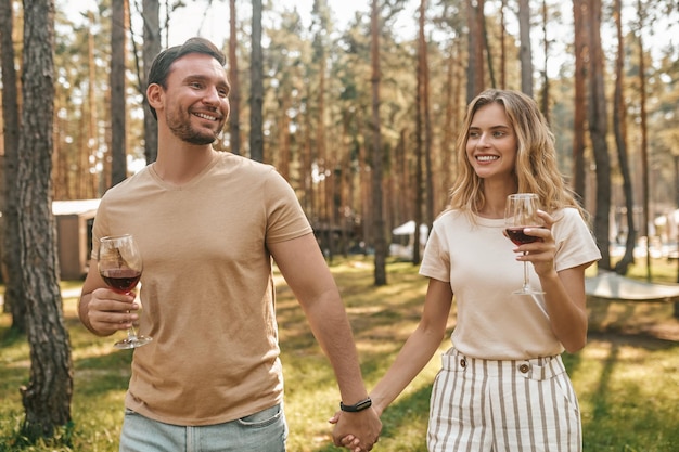 Bonito cara de cabelos escuros e uma linda senhora loira com copos de vinho tinto de mãos dadas