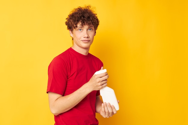 Bonito cara ruivo em detergentes de camiseta vermelha nas mãos posando fundo amarelo inalterado