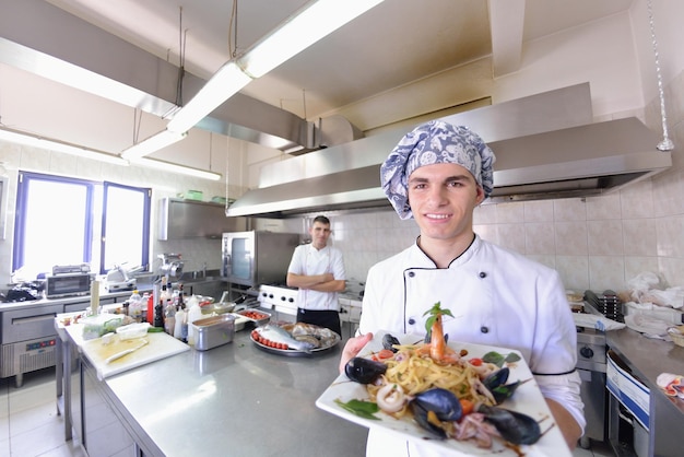 Bonito chef vestido de uniforme branco decorando salada de macarrão e frutos do mar na cozinha moderna