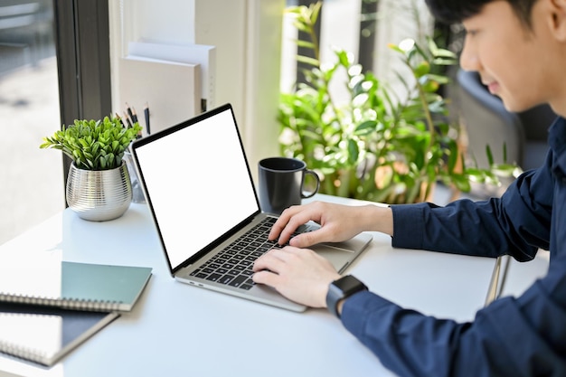 Bonito e focado jovem trabalhador asiático trabalhando em sua tarefa no computador portátil