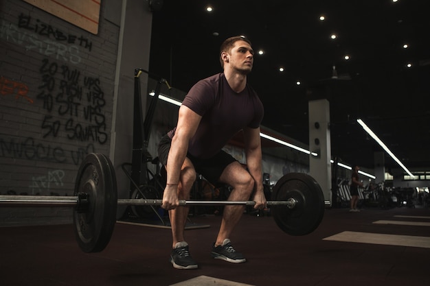 Foto bonito e jovem atleta do sexo masculino fazendo exercícios de levantamento terra no ginásio de treinamento funcional