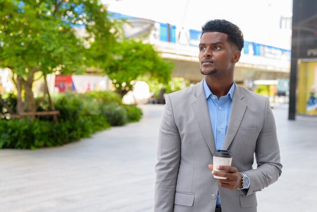 Bonito e jovem empresário africano ao ar livre carregando uma xícara de café para viagem enquanto pensa