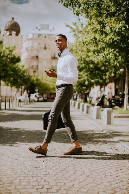 Bonito e jovem empresário afro-americano usando um telefone celular em uma rua