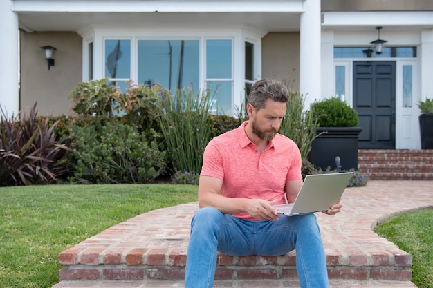 Bonito e jovem empresário sentado na escada enquanto usa seu laptop jovem homem de negócios ao ar livre.