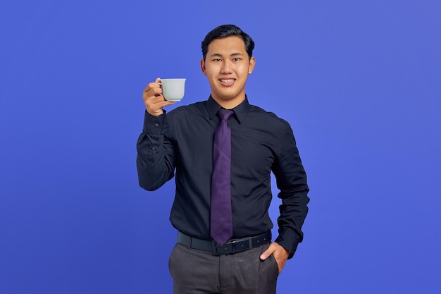 Bonito e jovem empresário sorrindo para a câmera com as mãos no bolso e segurando uma caneca