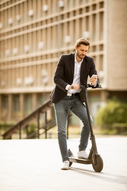 Bonito e jovem empresário usando o celular em uma scooter elétrica