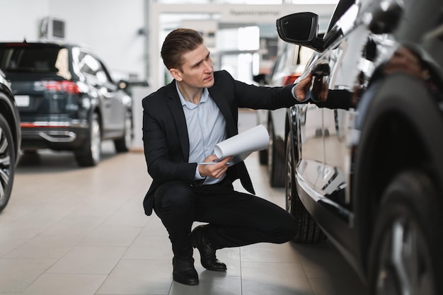 Bonito e jovem gerente de vendas fazendo um novo check-up de automóveis no salão de carros de luxo de corpo inteiro