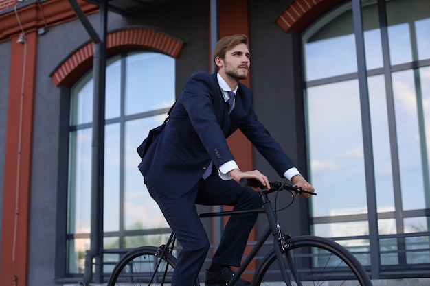 Bonito empresário andando de bicicleta para trabalhar na rua urbana de manhã.