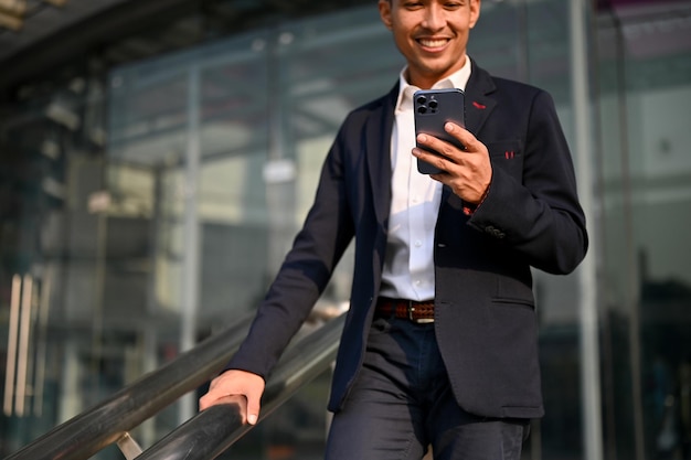 Bonito empresário asiático segurando seu smartphone enquanto descia as escadas em uma cidade