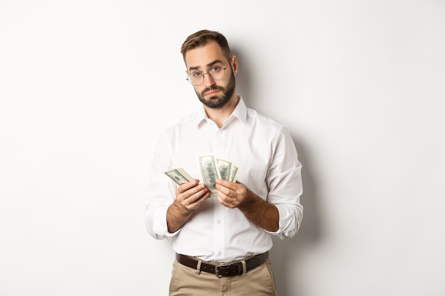 Bonito empresário contando dinheiro e olhando para a câmera, sério contra um fundo branco.