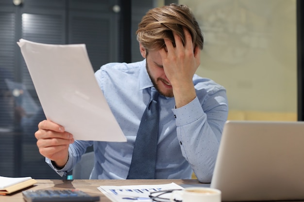 Bonito empresário estressado sentado à mesa em seu escritório.