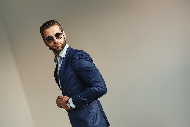 Bonito empresário no escritório barbudo homem sexy em um elegante terno e óculos de sol está de pé