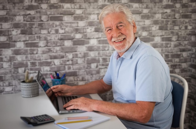 Bonito empresário sênior sentado no local de trabalho navegando no laptop homem barbudo idoso olhando para a câmera sorrindo