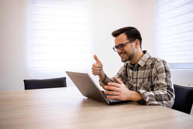 Bonito empresário trabalhando em seu computador portátil e tendo reunião online em seu escritório