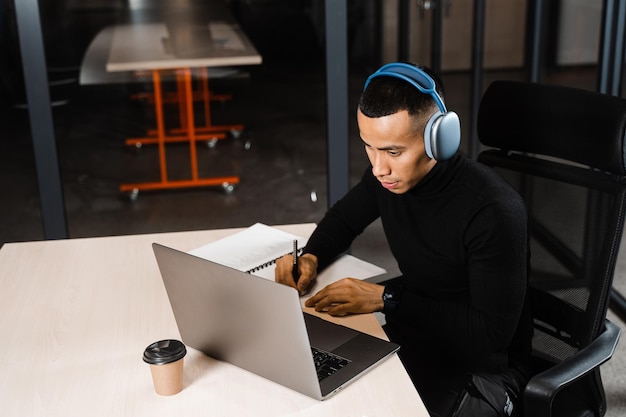 Bonito estudante asiático escreve notas e faz ensino à distância on-line Trabalho remoto para programadores com laptop e fones de ouvido