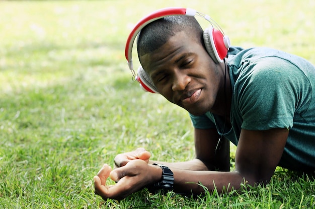 Bonito homem afro-americano com fones de ouvido deitado na grama verde