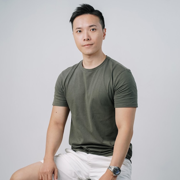 bonito homem asiático camiseta verde sorrindo sentado isolado na parede cinza