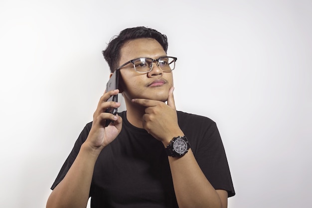 Foto bonito homem asiático chamando usando smartphone e mostrando expressão confusa no fundo branco