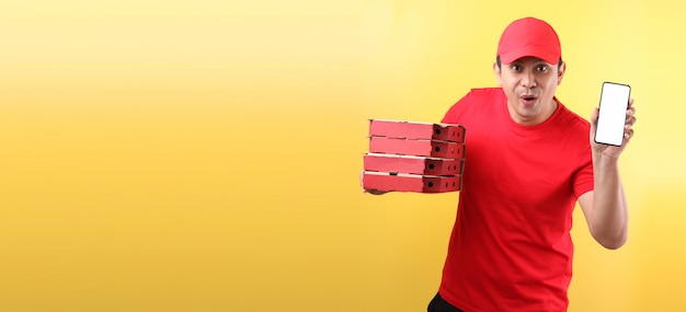 Foto bonito homem asiático de boné vermelho, dando comida italiana pizza em caixas de papelão isolado segurando o telefone móvel com tela vazia branca em branco.