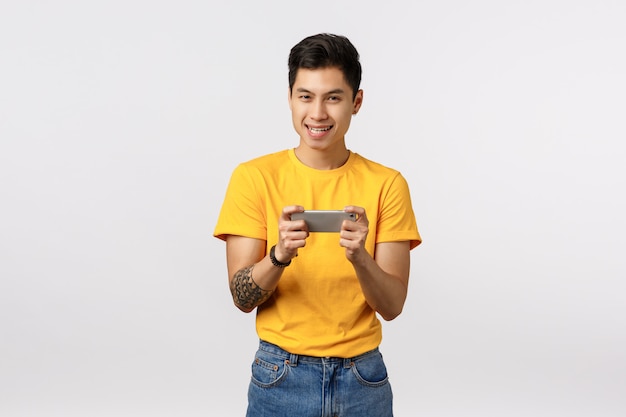 Bonito homem asiático de camiseta amarela, brincando com o smartphone